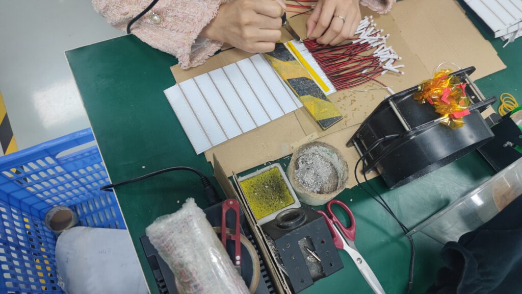 Worker soldering LED strip light components at an assembly workstation