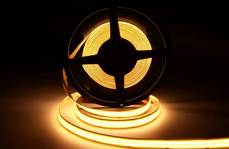 Warm white COB LED strip light glowing in a dark environment, partially unrolled from a black reel, ideal for ambient and decorative indoor lighting.