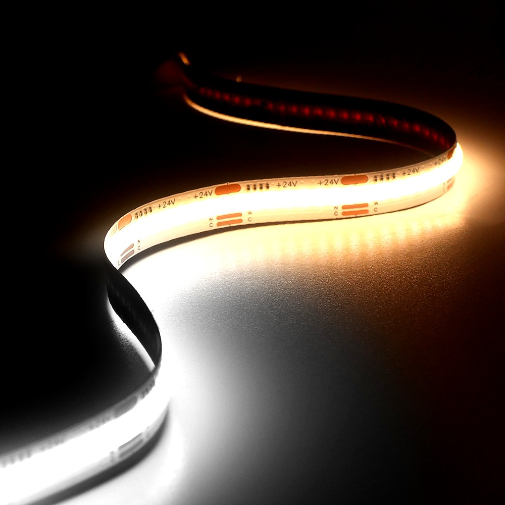 A 24V tunable white COB LED strip light glowing with dual CCT outputs, placed on a reflective surface, creating a gradient of warm and cool illumination.
