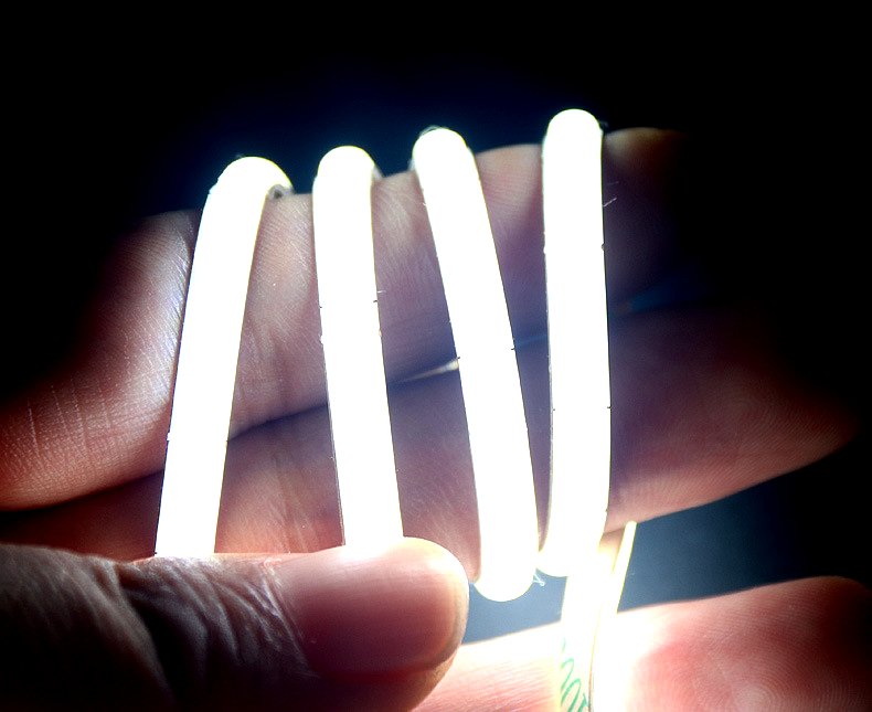 Close-up of a flexible COB LED strip glowing bright white while being held in hand, showcasing its bendable and soft-touch design for indoor lighting applications.