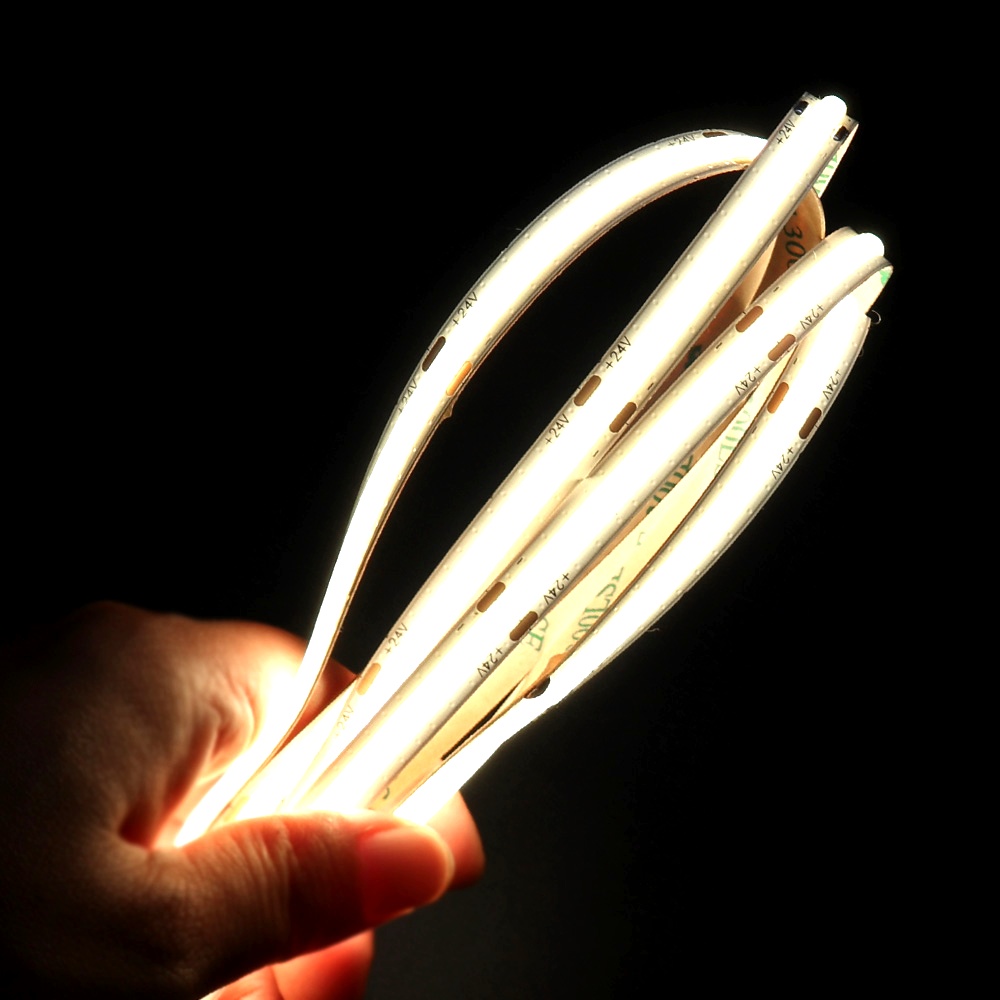 A hand holding flexible COB LED strip lights glowing brightly in the dark, showcasing bendable and uniform linear lighting