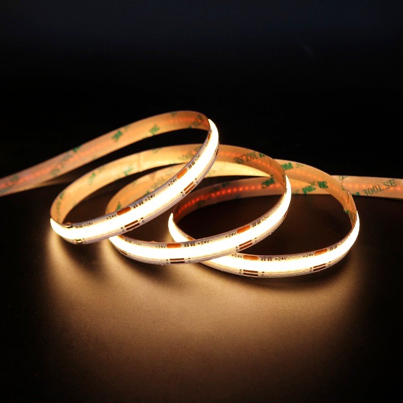 Close-up of a glowing warm white COB LED strip light arranged in curves on a dark background, featuring 3M adhesive backing