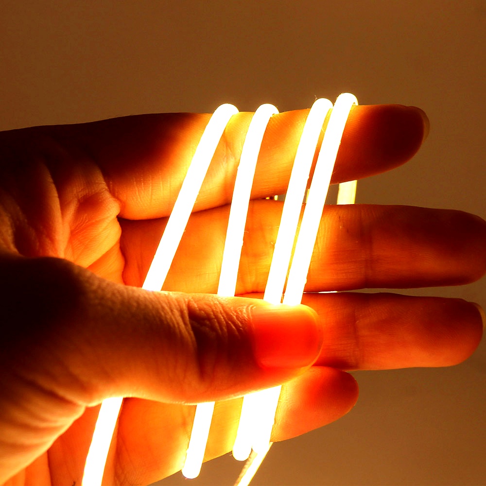 Close-up of a hand holding a flexible warm white COB LED strip light, demonstrating safe touch and bendability for versatile lighting installations