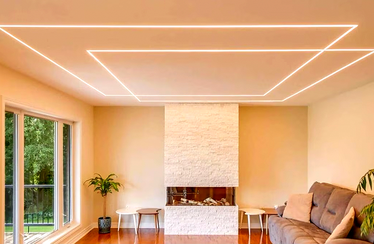 Modern living room with recessed LED strip lights installed in linear patterns on the ceiling, creating a soft ambient lighting effect above a fireplace and sofa