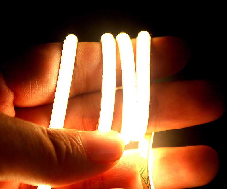 A hand holding flexible COB LED strip light glowing in warm white color