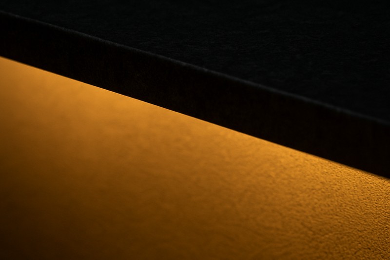 The edge of a dark stone countertop is clearly defined by a subtle line of warm light from an under-mounted LED strip.