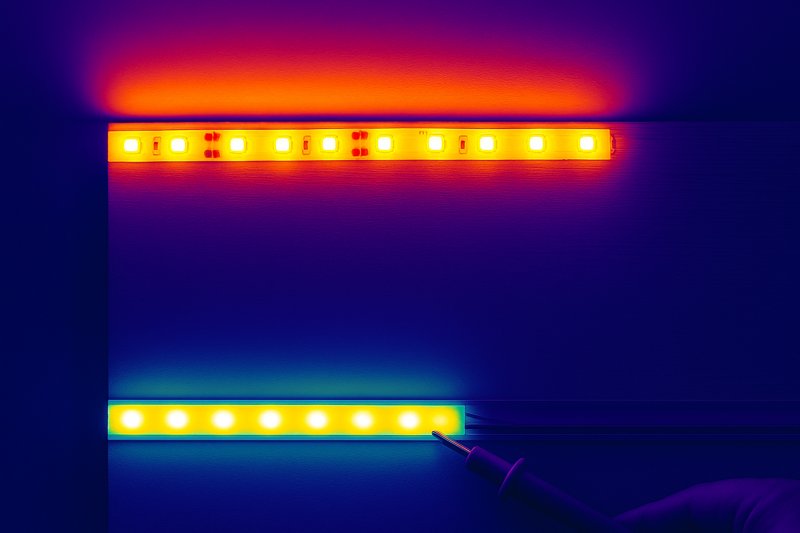 A thermal camera image showing two LED strips: one mounted on wood glowing red-hot, and another in an aluminum channel appearing much cooler in blue/green.