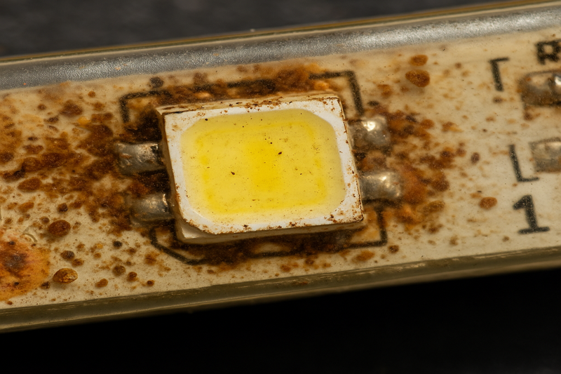 A close-up macro photo showing a corroded LED chip and circuit board inside a water-damaged strip light