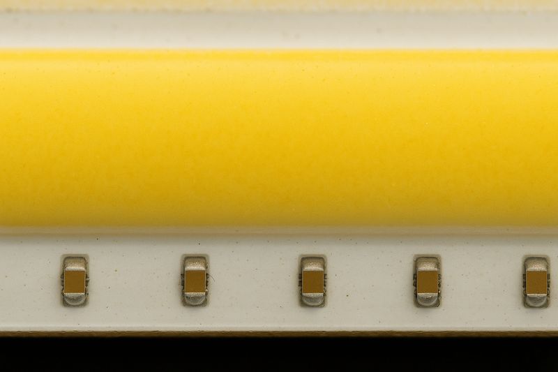A macro close-up shot of a COB LED strip, showing the continuous yellow phosphor line with the tiny chips barely visible underneath.